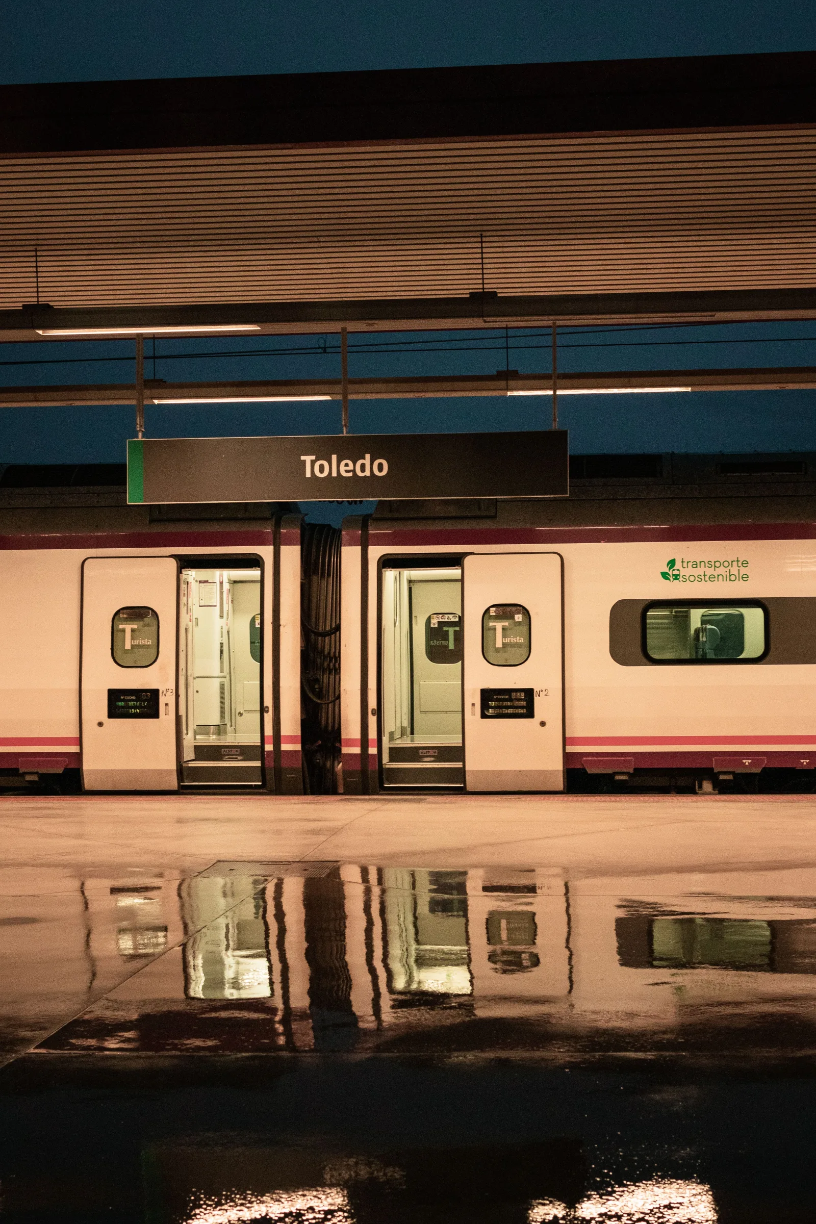 Andén de la estación de tren de Toledo, con un tren y reflejos. Escena de transporte urbano por la noche.