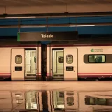 Andén de la estación de tren de Toledo, con un tren y reflejos. Escena de transporte urbano por la noche.