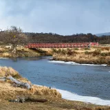 Vista pintoresca de un río y un puente rojo en Puerto Almanza, Argentina, bajo un cielo nublado.