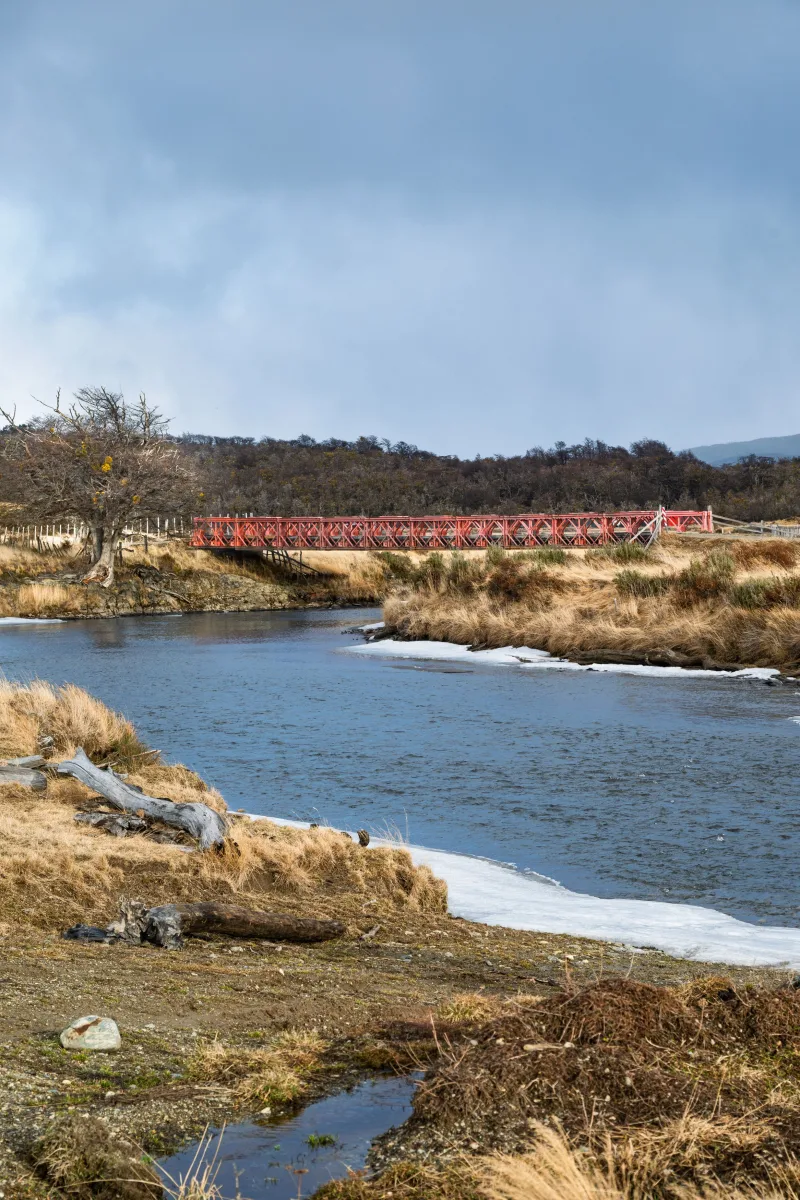 Vista pintoresca de un río y un puente rojo en Puerto Almanza, Argentina, bajo un cielo nublado.
