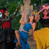 Vibrant Día de Muertos celebration featuring women in traditional Catrina attire at a cemetery.