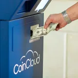 Una mano introduce efectivo en un cajero automático de CoinCloud, ilustrando el proceso de intercambio de criptomonedas.