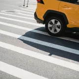 Un automóvil amarillo moderno circula por un paso de peatones en una calle de la ciudad en un día soleado.