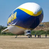 The iconic Goodyear blimp parked in a sunny outdoor setting with a few people nearby.