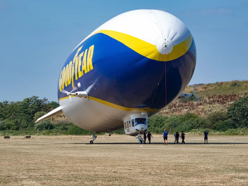 The iconic Goodyear blimp parked in a sunny outdoor setting with a few people nearby.