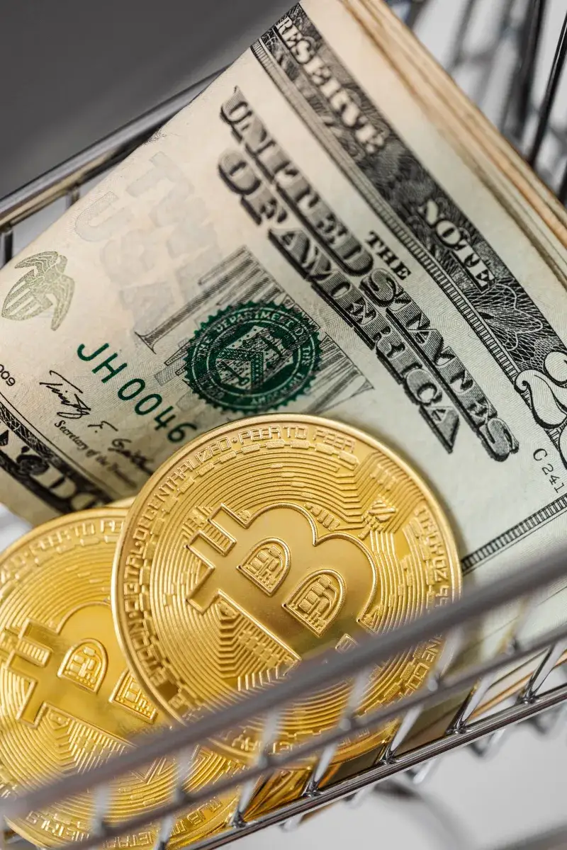 Gold bitcoins and US dollar bills in a small shopping cart representing finance and digital currency.