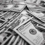 Imagen monocromática de billetes de cien dólares de Estados Unidos dispersos, que representan la riqueza y la prosperidad.