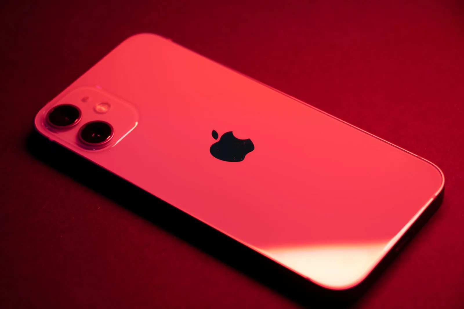 Primer plano de un teléfono inteligente rojo con doble cámara sobre un fondo rojo, que destaca por su diseño elegante y tecnología.