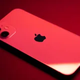 Primer plano de un teléfono inteligente rojo con doble cámara sobre un fondo rojo, que destaca por su diseño elegante y tecnología.