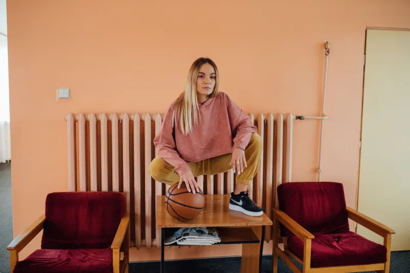 Young woman dressed in sporty attire holding a basketball indoors, expressing a casual yet confident style.