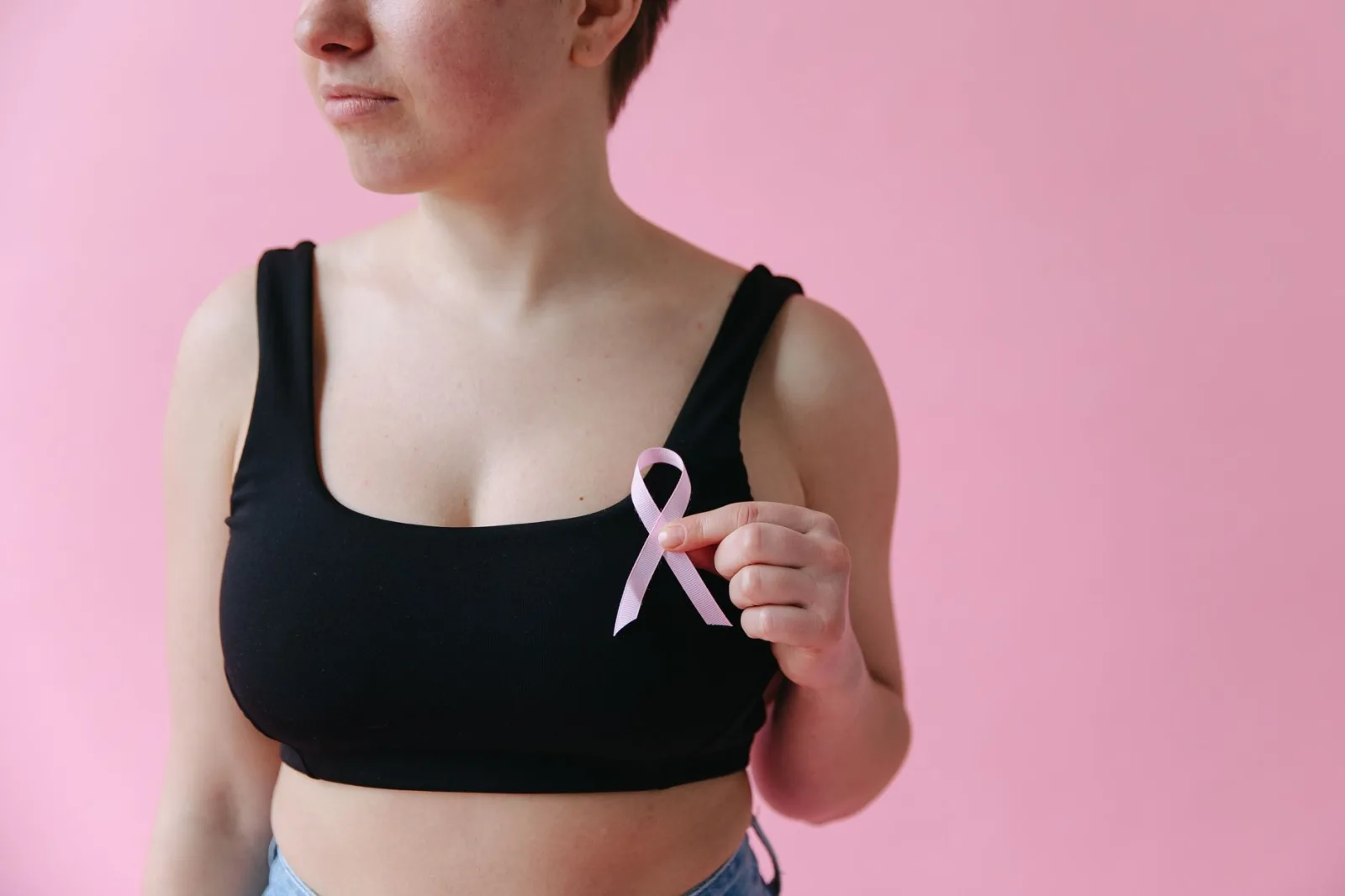 Primer plano de una mujer sosteniendo un lazo rosa que simboliza la concienciación sobre el cáncer de mama.