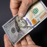 Detailed image of hands exchanging a crisp one hundred dollar bill, symbolizing financial transactions.