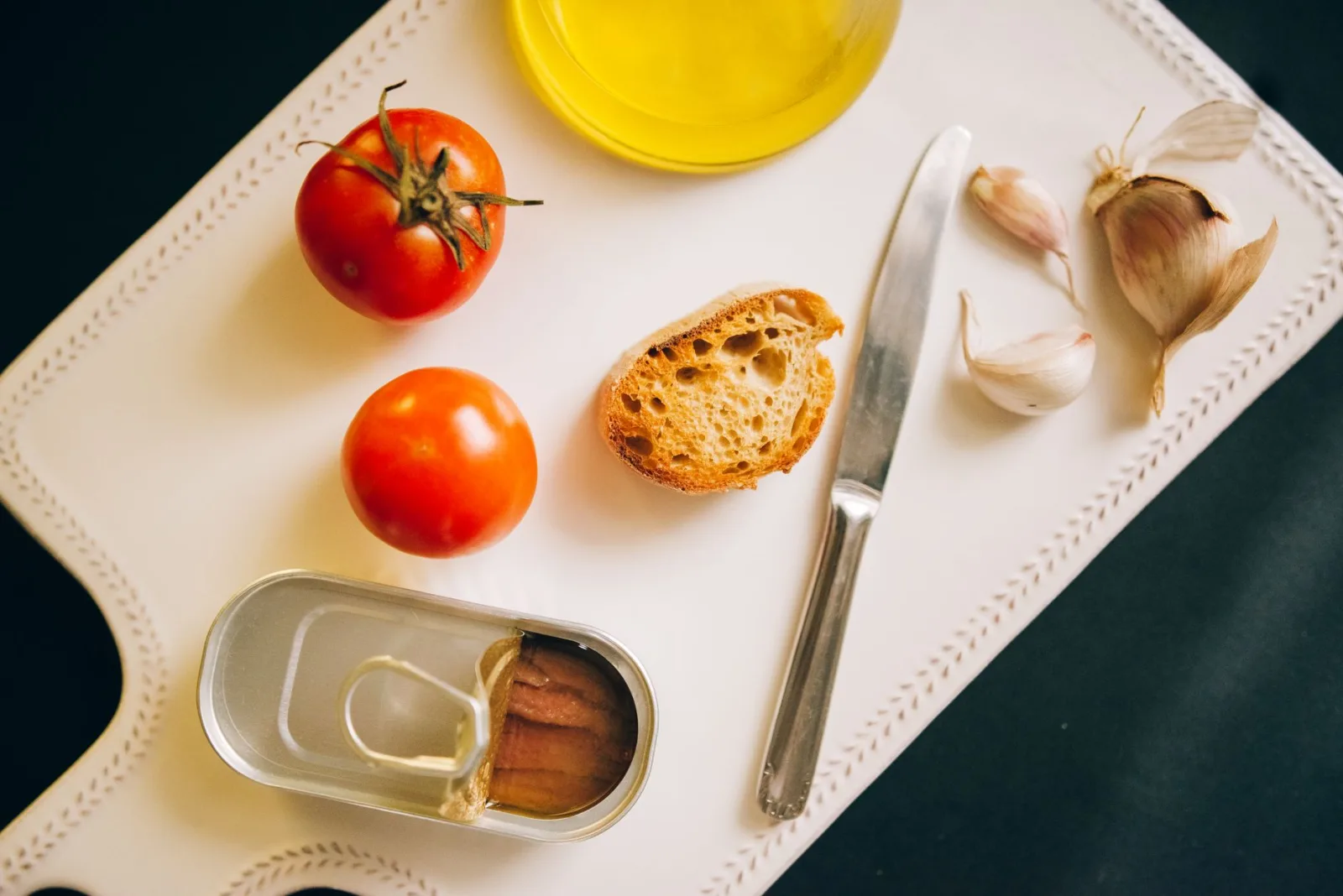 Tomatoes, bread, and sardines arranged for Catalán toast preparation.