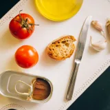 Tomatoes, bread, and sardines arranged for Catalán toast preparation.