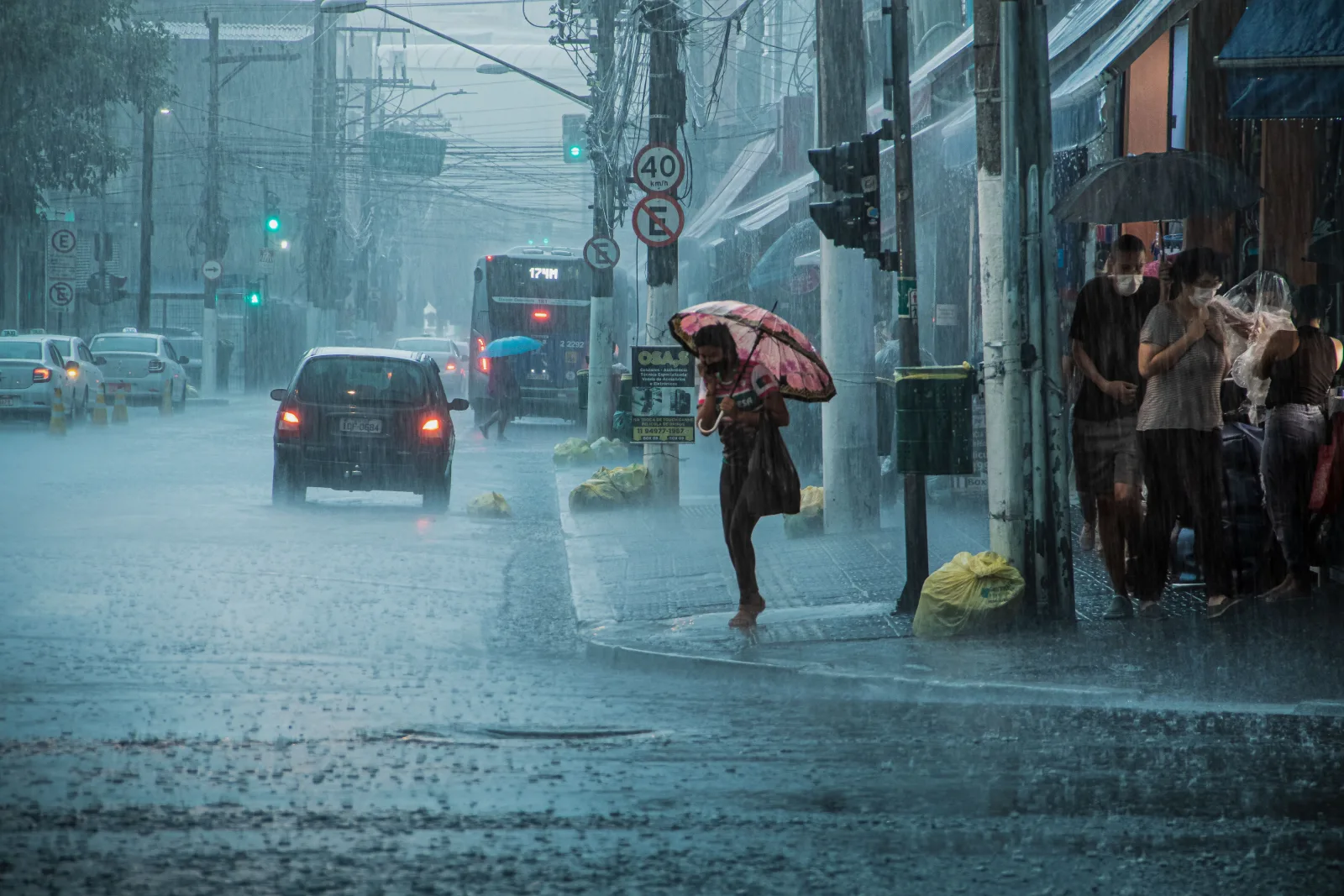 Una calle urbana concurrida bajo lluvia intensa, con autos, peatones y paraguas.