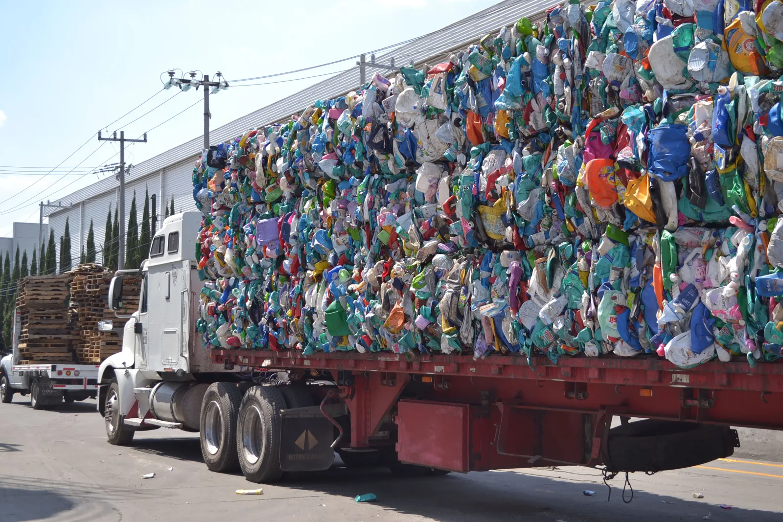 Un camión grande que transporta fardos de residuos plásticos comprimidos por una calle soleada de una ciudad de México.