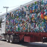 Un camión grande que transporta fardos de residuos plásticos comprimidos por una calle soleada de una ciudad de México.