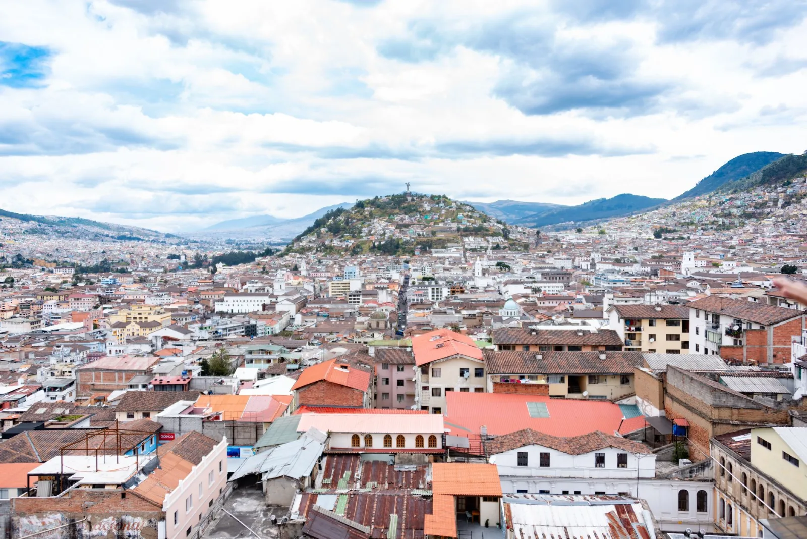 Vista aérea que muestra el paisaje urbano de Quito con colinas ondulantes y techos coloridos.