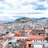Vista aérea que muestra el paisaje urbano de Quito con colinas ondulantes y techos coloridos.