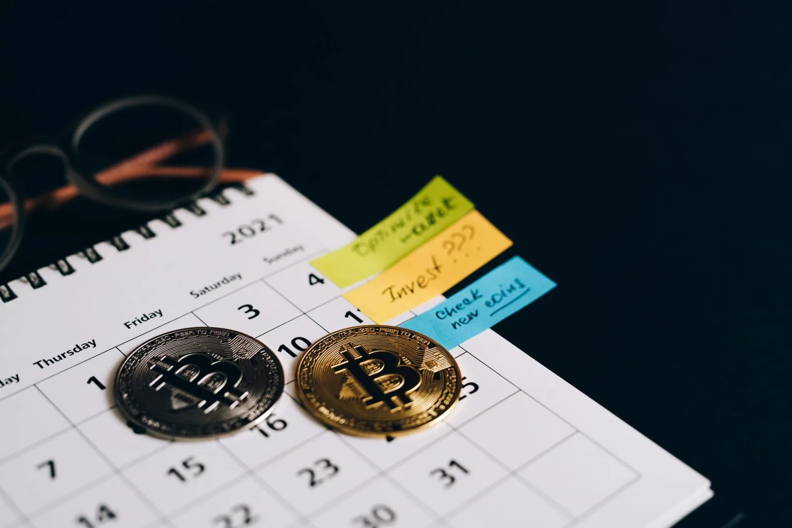 Monedas de bitcoin sobre un calendario con notas adhesivas para planificar inversiones.