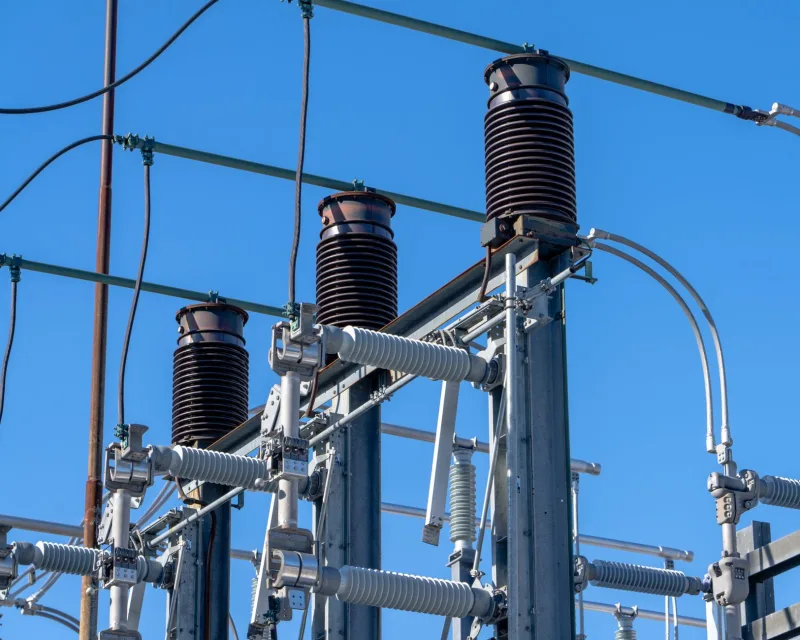 Detailed view of electrical components in a power substation under a clear blue sky.