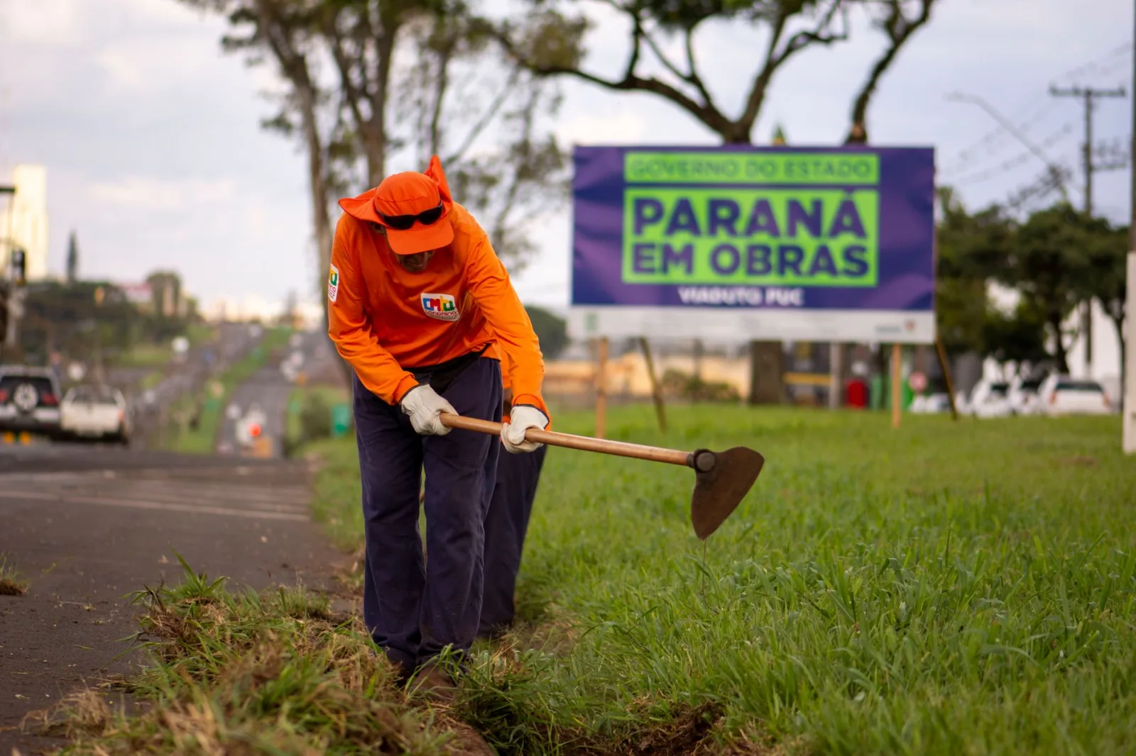 Un trabajador con uniforme naranja mantiene el césped al borde de la carretera en Londrina, Brasil.