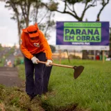 Un trabajador con uniforme naranja mantiene el césped al borde de la carretera en Londrina, Brasil.