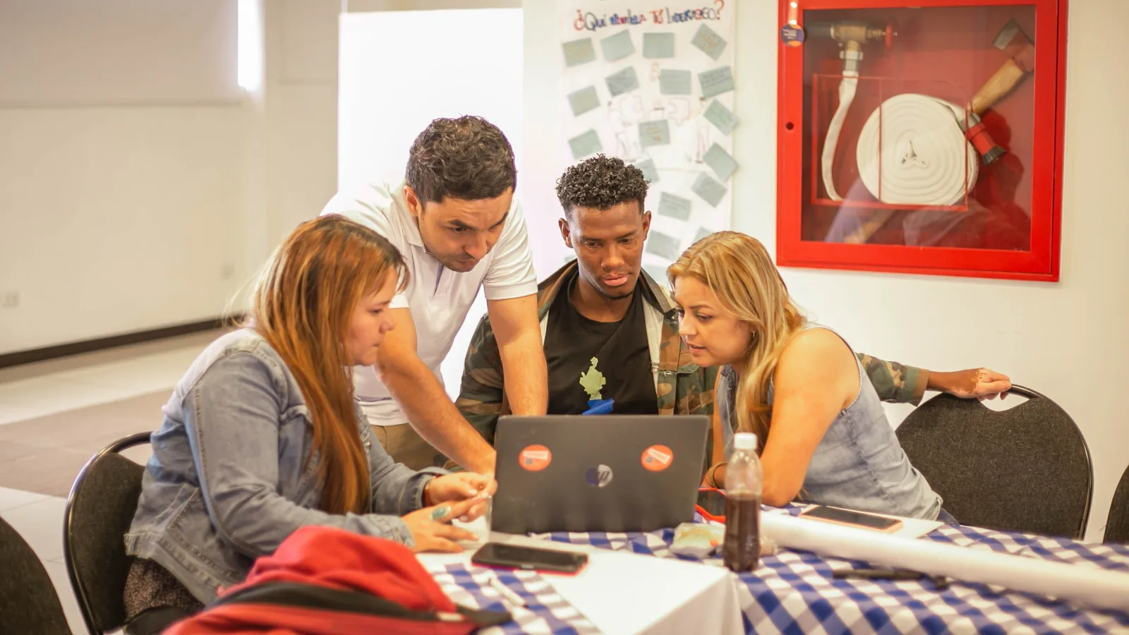 Un grupo diverso de adultos colabora alrededor de una computadora portátil durante una reunión de equipo en un entorno profesional.