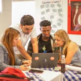 Un grupo diverso de adultos colabora alrededor de una computadora portátil durante una reunión de equipo en un entorno profesional.