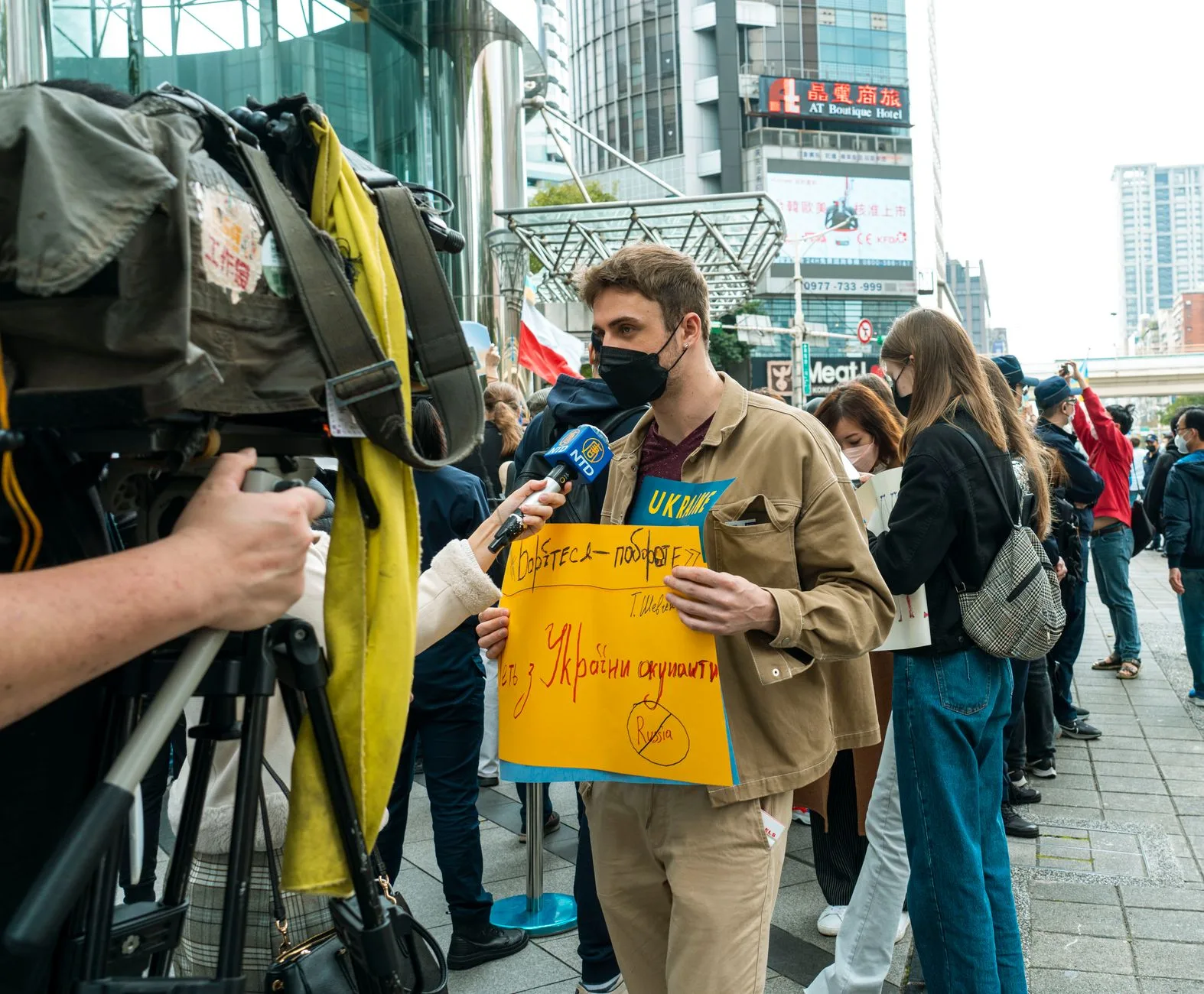 Un joven sostiene un cartel de protesta durante una manifestación callejera contra la guerra, cubierta por los medios de comunicación.