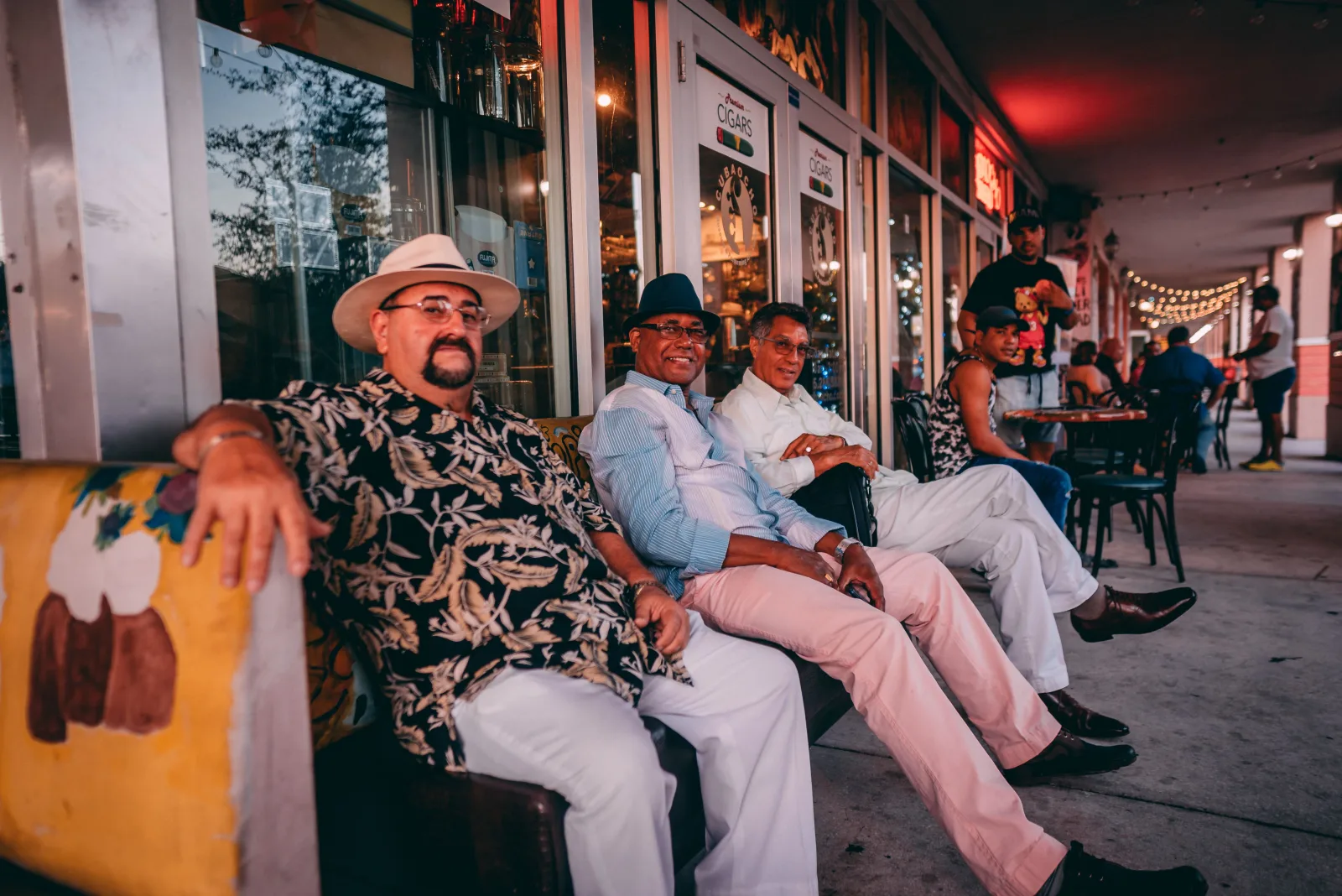 Un grupo de hombres se sienta a disfrutar de una velada relajada al aire libre, frente a una cafetería de Miami.