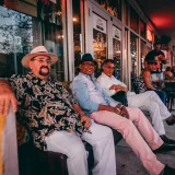 Un grupo de hombres se sienta a disfrutar de una velada relajada al aire libre, frente a una cafetería de Miami.