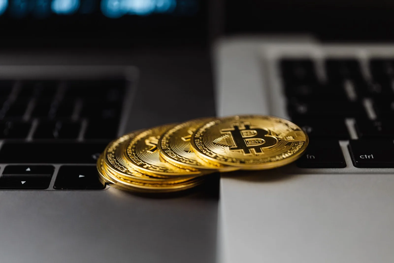 Primer plano de monedas doradas de Bitcoin sobre teclados de portátiles, que representan la moneda digital y la riqueza.