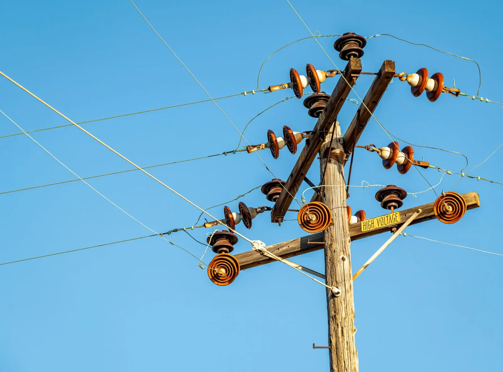 Línea eléctrica de alta tensión y aisladores fotografiados sobre un cielo azul despejado.