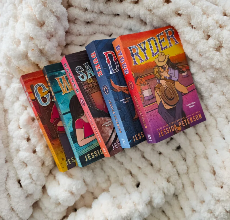 A vibrant collection of romance novels by Jessica Peterson resting on a plush white blanket, creating a cozy reading vibe.