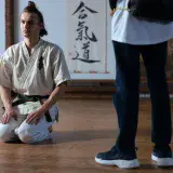 Martial artist in traditional training attire kneeling in a dojo, focused and poised.