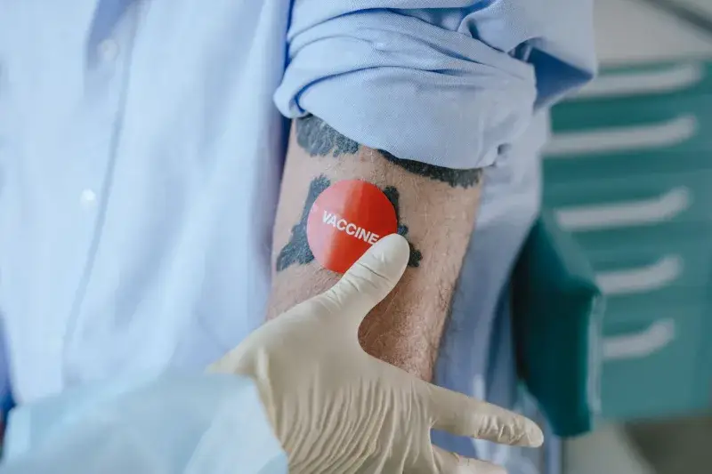 A healthcare professional applies a vaccine sticker on a tattooed arm in a medical environment.