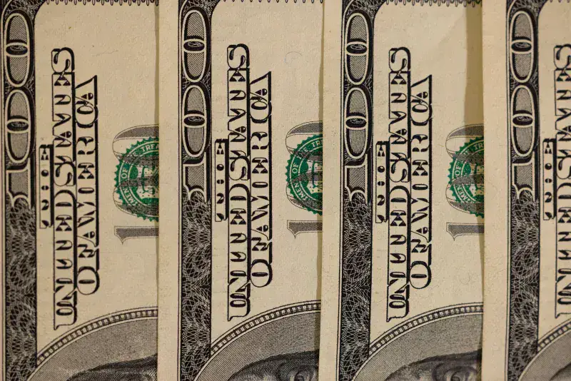 Detailed close-up of multiple US hundred dollar bills, showcasing currency design.