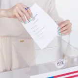 Una persona depositando su voto en una urna transparente durante unas elecciones.