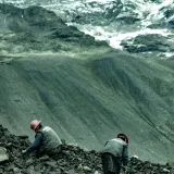 Dos mineros en Perú excavan entre montones de rocas en los Andes en busca de oro, bajo montañas nevadas.