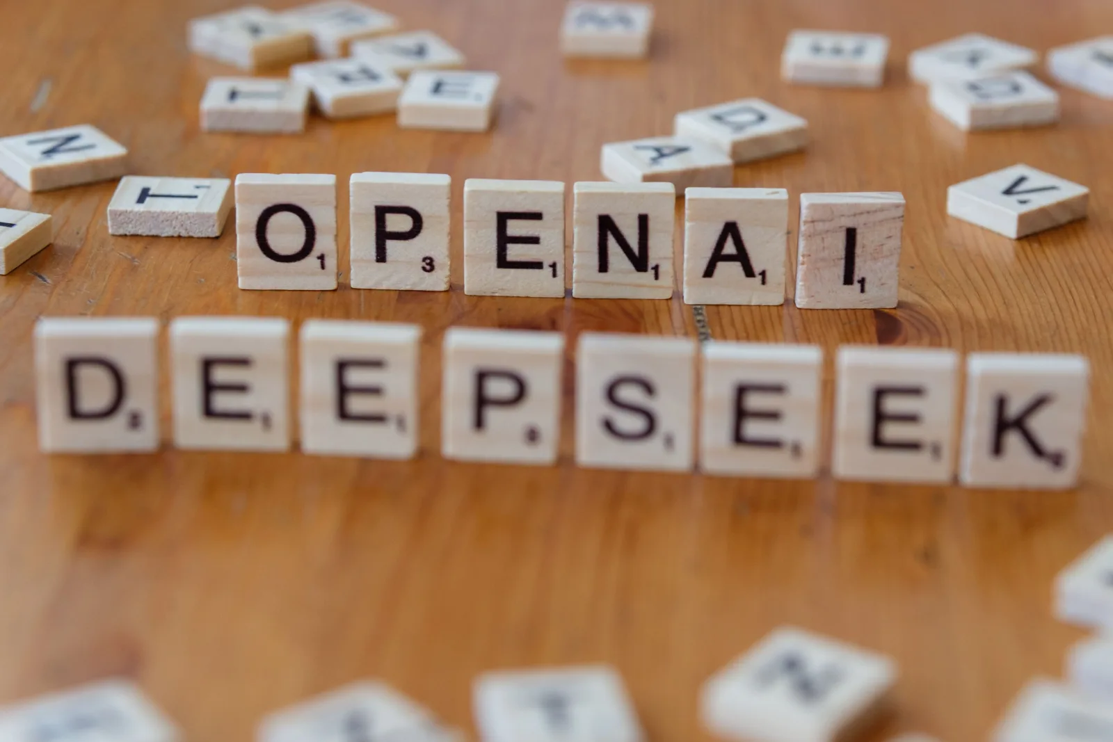 Primer plano de fichas de Scrabble de madera que deletrean OpenAI y DeepSeek sobre una mesa de madera.