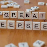 Primer plano de fichas de Scrabble de madera que deletrean OpenAI y DeepSeek sobre una mesa de madera.