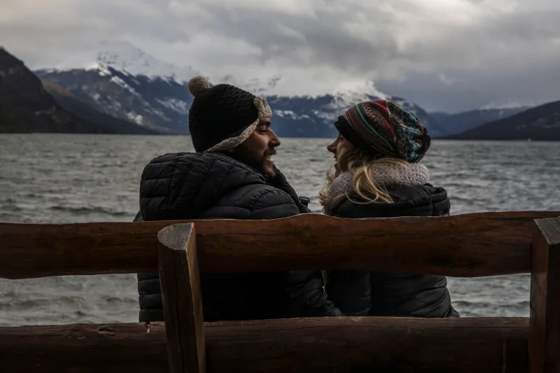 Couple sitting on a wooden bench by the lake in Tierra del Fuego, Argentina.