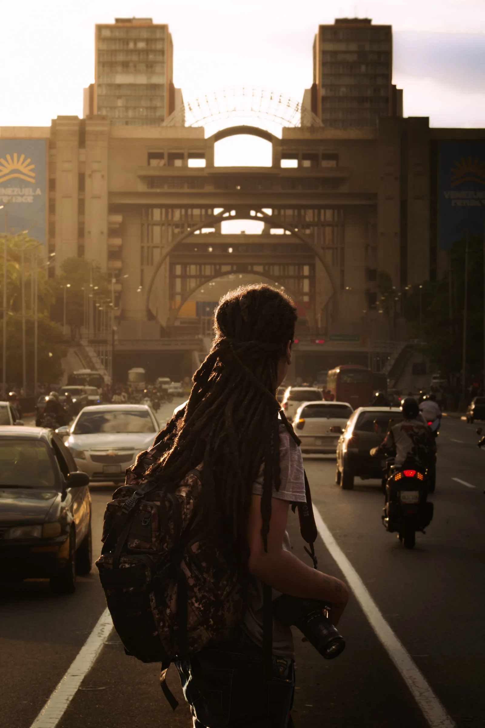 Persona con rastas y mochila caminando por una calle concurrida de Caracas al atardecer.