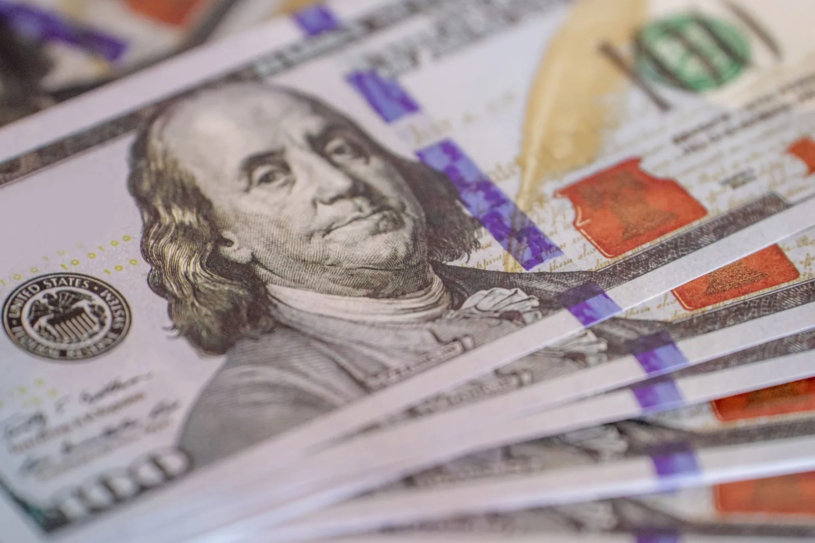 Primer plano detallado de billetes de cien dólares estadounidenses desplegados en abanico, que muestra los detalles de la moneda.
