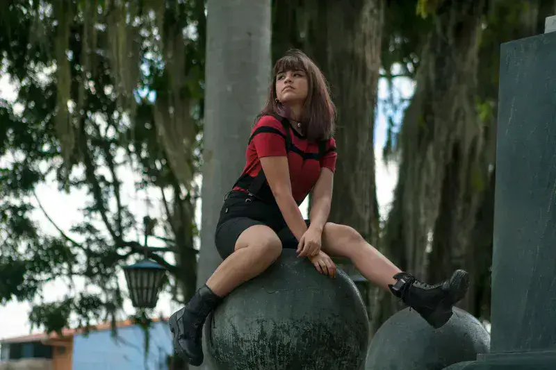 Young woman in stylish outfit sitting outdoors on a large sphere in Venezuela.