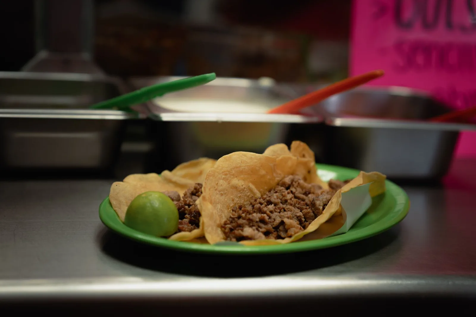Primer plano de unos deliciosos tacos de carne con lima, servidos en un plato verde en un restaurante mexicano.