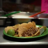 Primer plano de unos deliciosos tacos de carne con lima, servidos en un plato verde en un restaurante mexicano.