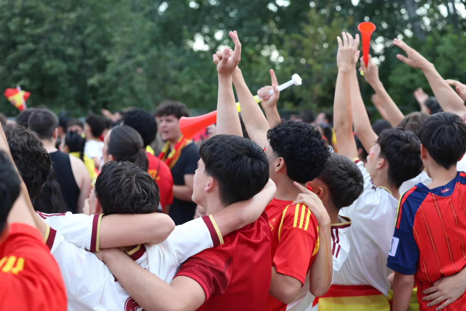 Grupo de aficionados al fútbol entusiastas celebrando una victoria en Madrid, abrazándose y vitoreando al aire libre.