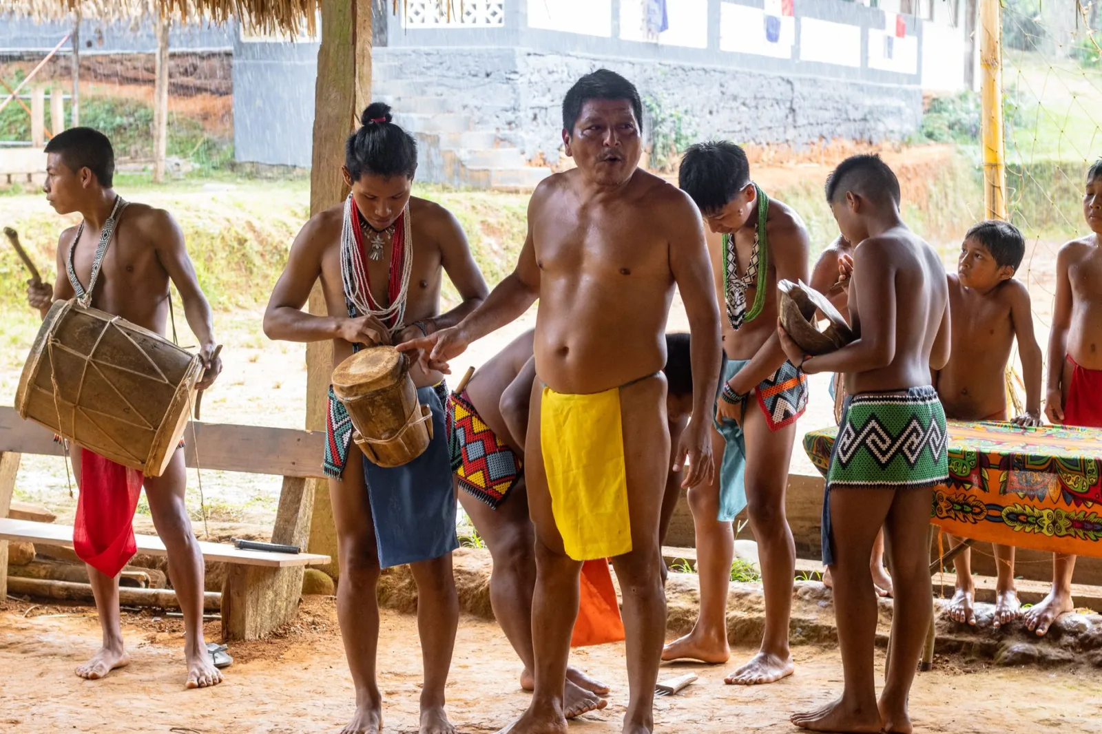 Grupo de hombres y niños indígenas tocando instrumentos tradicionales al aire libre y celebrando su herencia cultural.